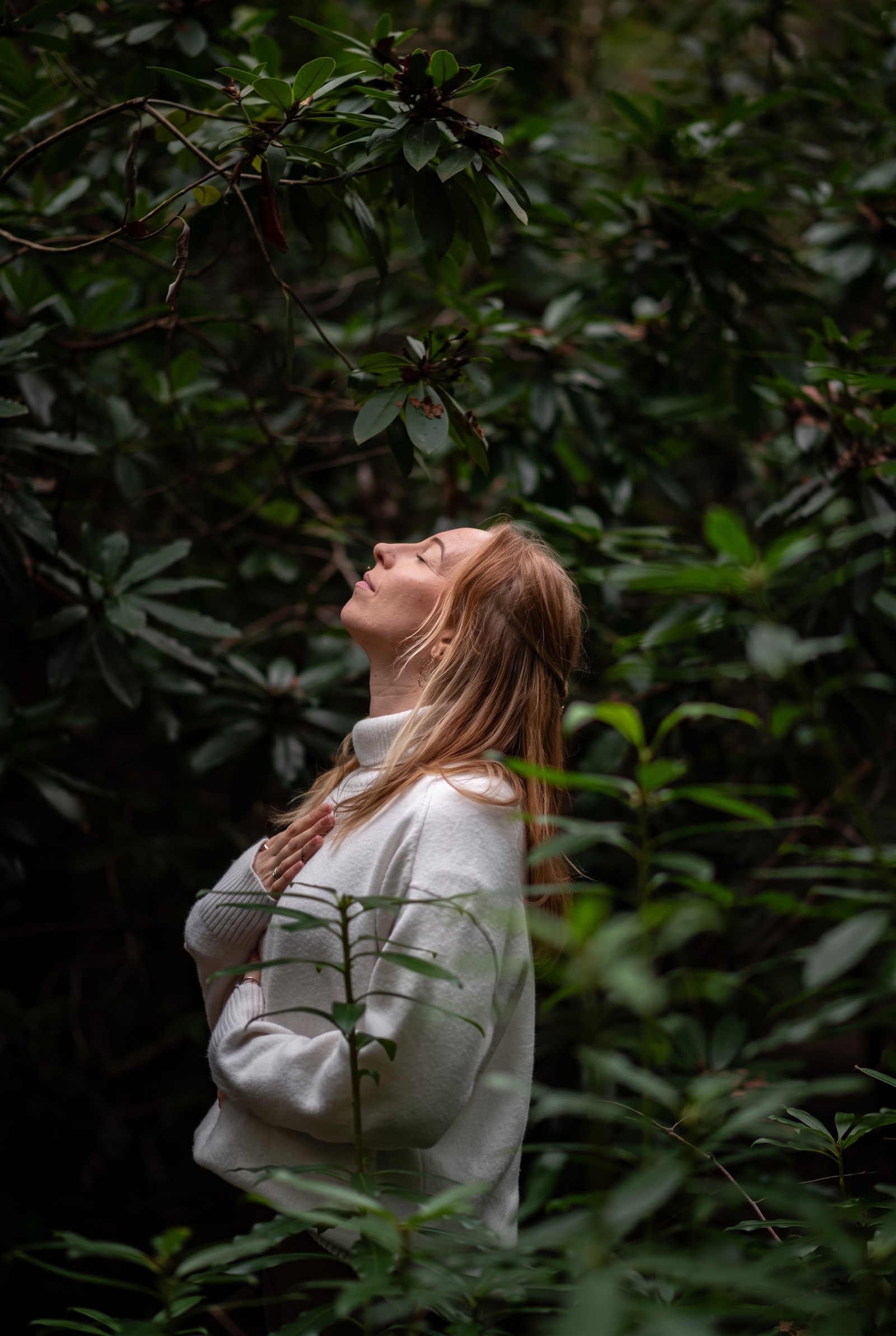 Lottie standing among deep green foliage with her hand over her heart, face turned to the light